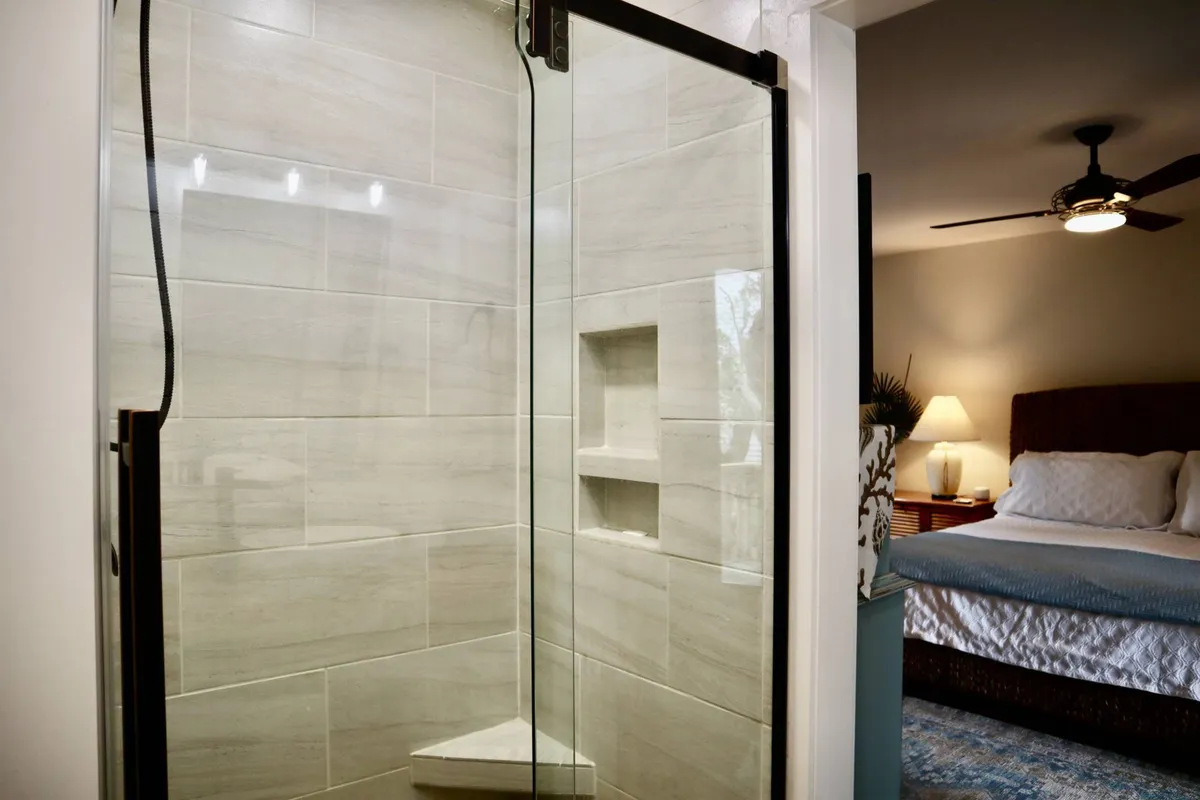 A modern bathroom with a sleek glass shower enclosure, contemporary tile design, and soft lighting extending into the adjacent bedroom. The space feels spa-like and serene, inviting guests to unwind.