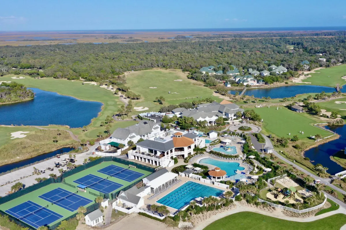 A broad view of a luxurious community area featuring a golf course, multiple swimming pools, tennis courts, and a clubhouse. The scene is lively and upscale, encapsulating the exclusive amenities offered with optional BHI Club access.