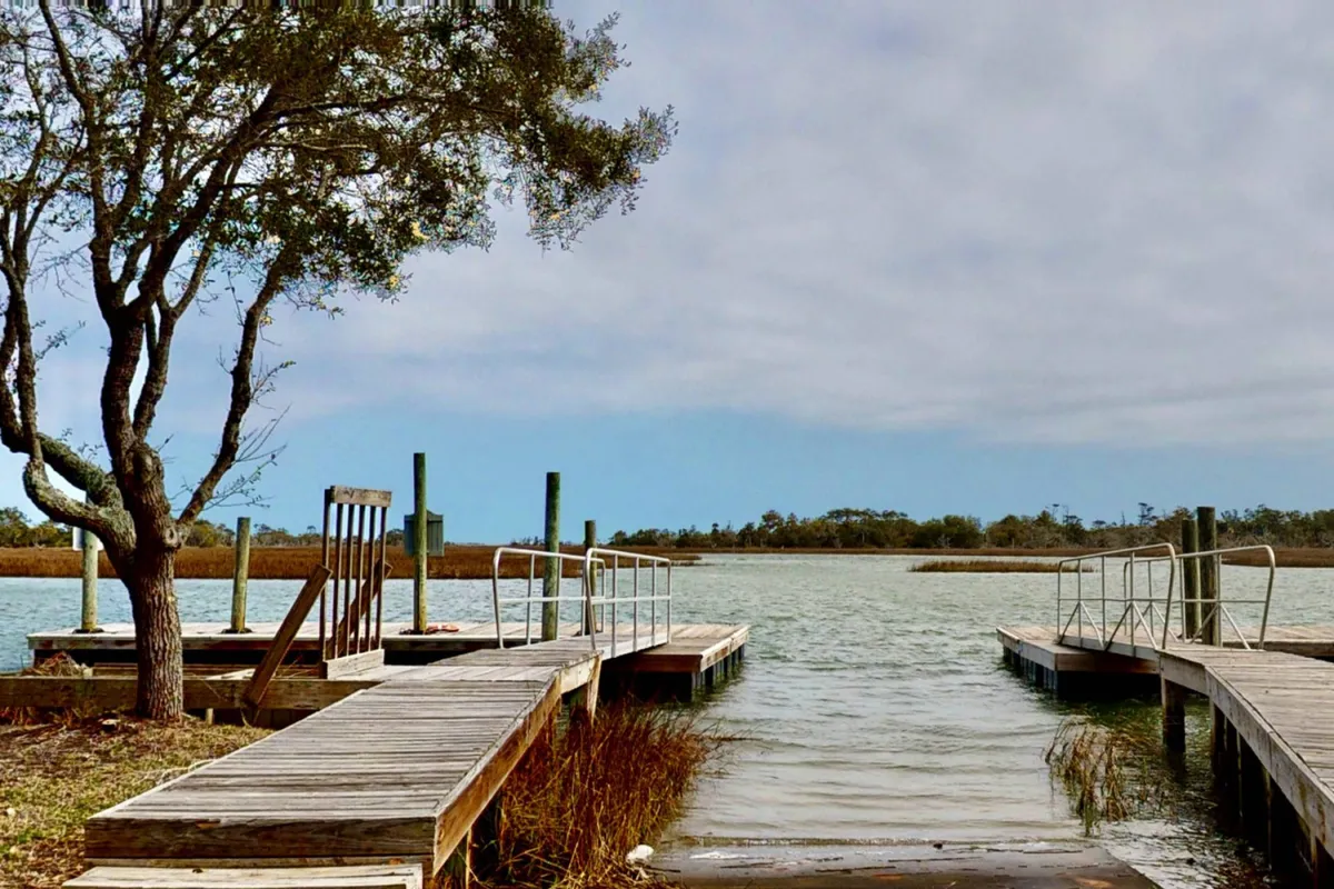A peaceful scene featuring wooden docks extending over calm water, framed by trees and gentle foliage. The area is ideal for fishing, boating, or simply relaxing by the water, capturing the community dock experience.