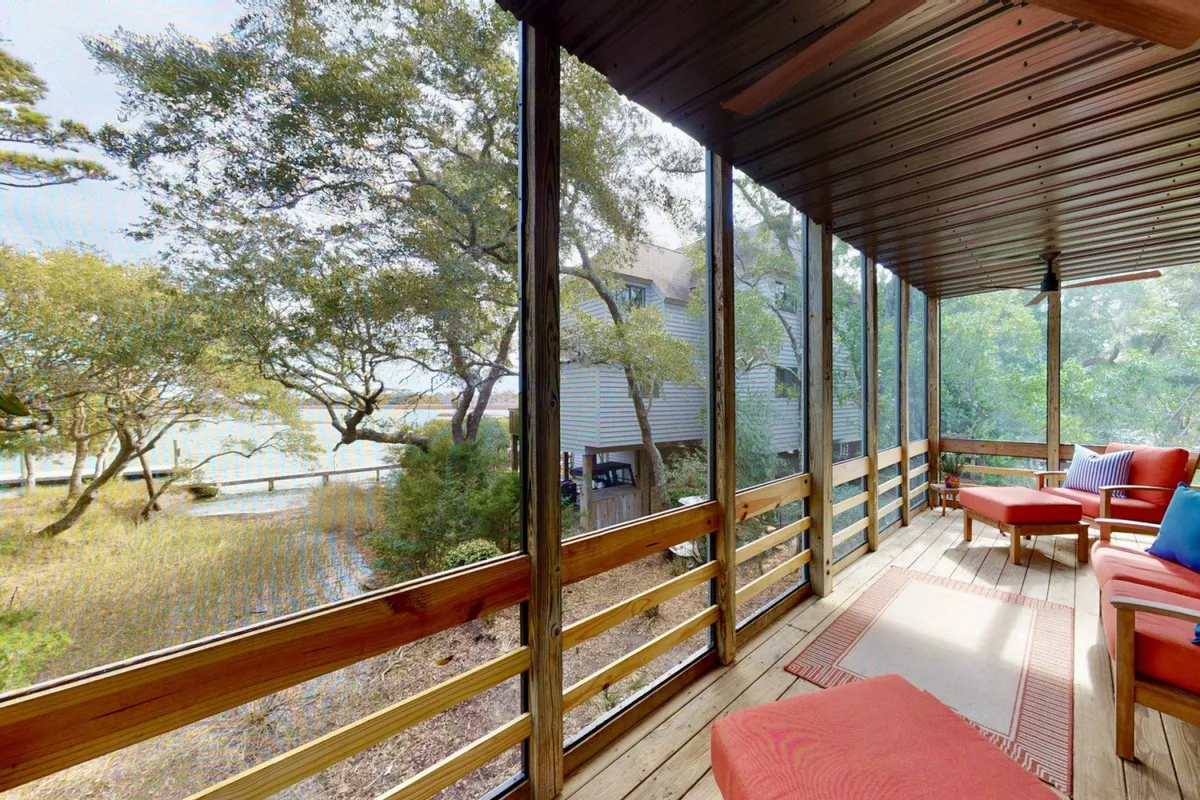 A tranquil screened porch with cozy seating overlooks the serene marshland and water. The seating area is designed for comfort, inviting guests to relax while enjoying the protected outdoor space and breathtaking natural vistas.